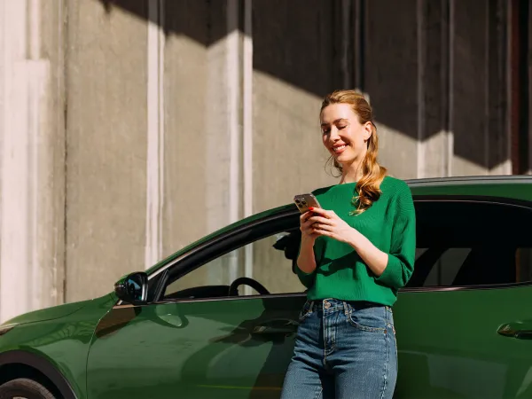 Nainen puhelimella nojailemassa autoon.
